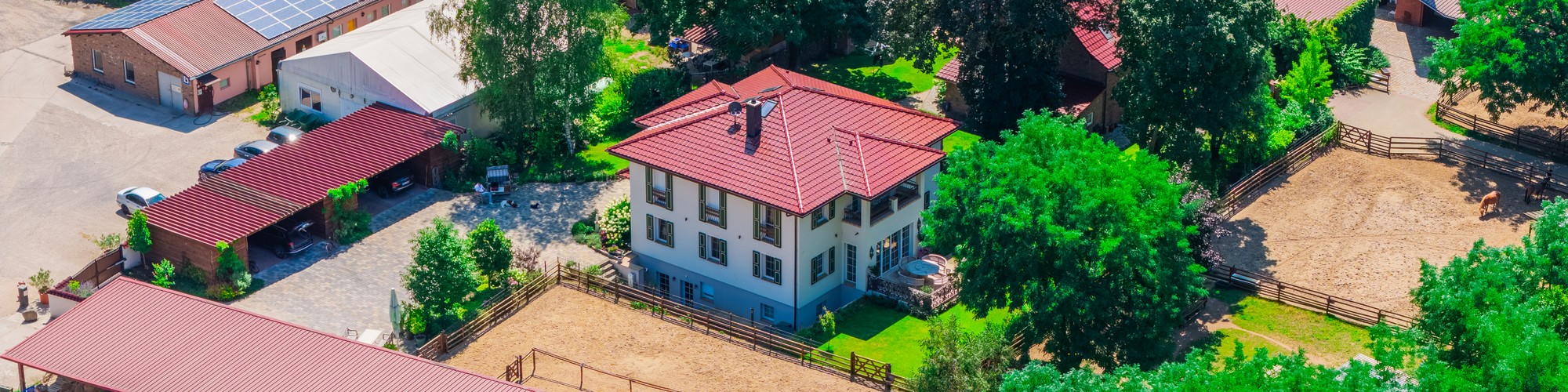 Luftaufnahme: frei geplante Stadtvilla mit rotem Walmdach auf einem Reiterhof in Brandenburg